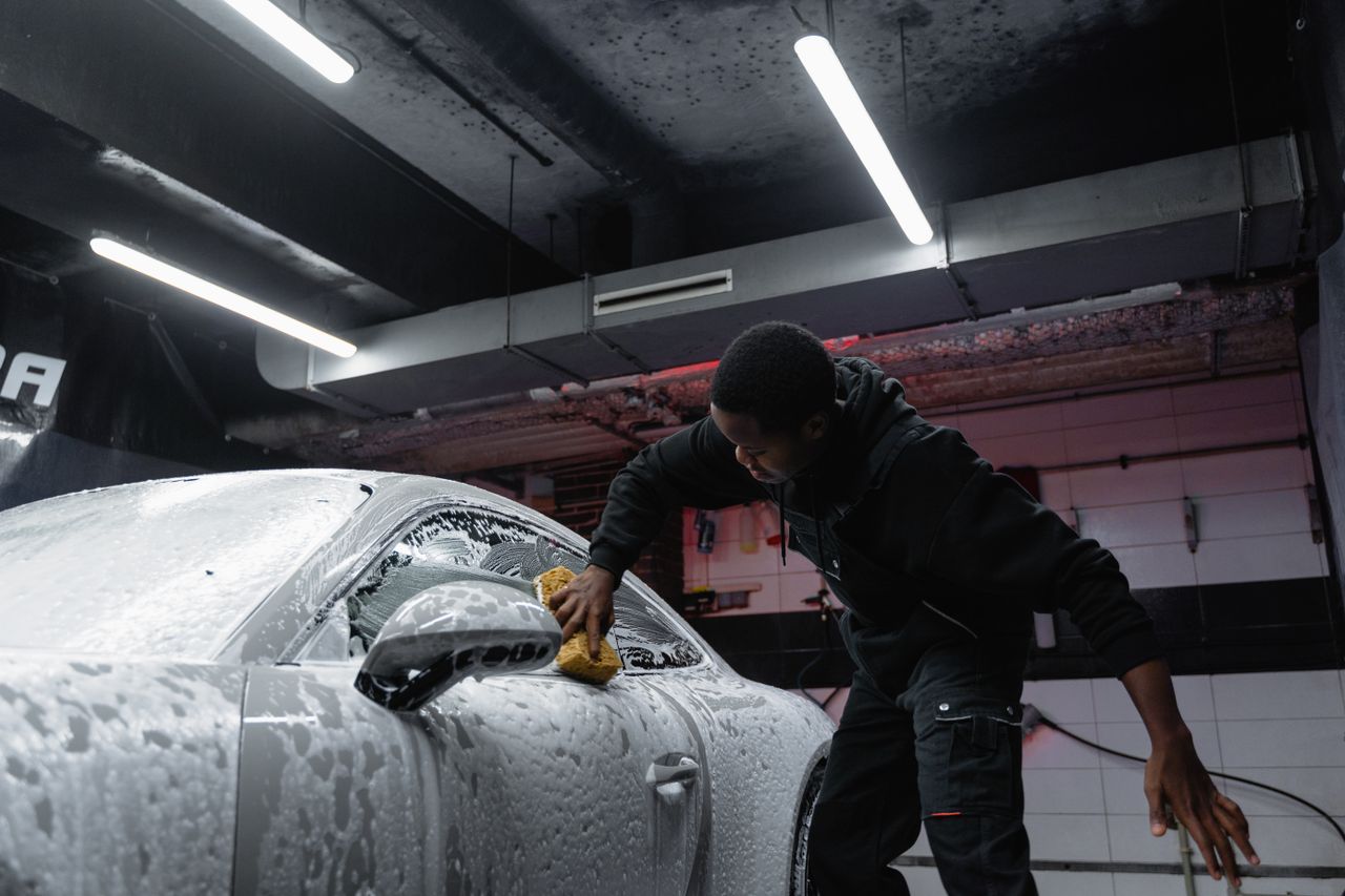 Man cleaning a car with soap and sponge at an indoor carwash facility.