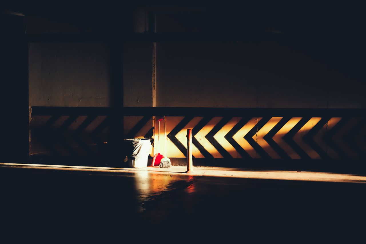 Contrasting sunlight illuminating a broom and bucket in dramatic urban interior.