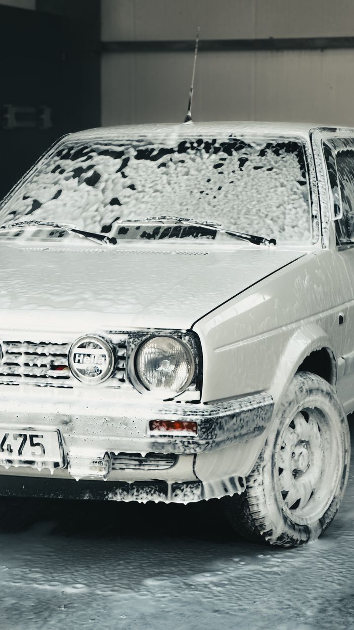 Classic car covered in soap foam during a wash at an indoor car wash facility.